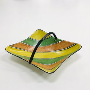 Op de afbeelding: Een vierkante serveerschaal van keramiek met een zwarte handgreep. De schaal is versierd met gele, groene en bruine strepen.
