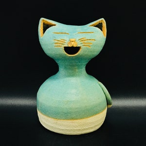 Peut inclure: Une figurine de chat en céramique avec un glaçage bleu clair et une base blanche. Le chat a une grande bouche ouverte et une expression joyeuse.
