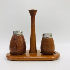 Könnte beinhalten: Ein Salz- und Pfefferstreuer-Set aus Holz mit einem Ständer. Die Streuer sind braun und haben silberne Oberteile. Der Ständer ist ebenfalls braun und hat eine erhöhte Mitte.