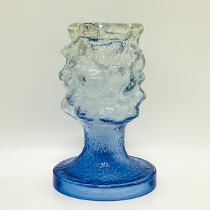 May include: A blue and clear glass candle holder with a textured, organic design. The holder has a wide base and a narrow top.