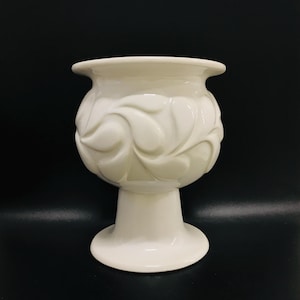 Peut inclure: Pot en céramique blanche avec une base en piédestal et un motif de feuilles stylisées.