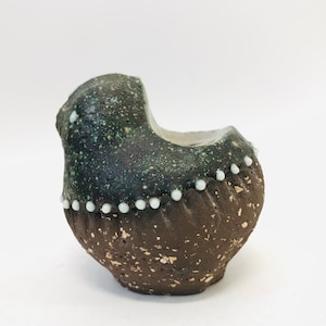 May include: A small, brown ceramic planter with a green glaze and white dots around the rim. The planter has a unique, asymmetrical shape.
