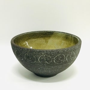 May include: A dark gray ceramic bowl with a green glaze inside. The bowl has a textured exterior with a repeating pattern of circles around the rim.