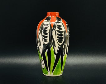 Peut inclure: Un vase en céramique blanche avec un motif abstrait rouge, noir et vert. Le motif représente deux figures avec des contours noirs et des accents verts.