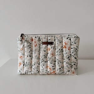 May include: A white quilted makeup bag with a floral print and a brown leather tag that says "MORRIS & SONS".