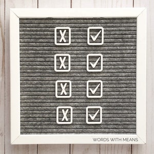 May include: A white letter board with a gray felt background. The board has four rows of white squares with either a checkmark or an X inside each square. The bottom of the board says "WORDS WITH MEANS".