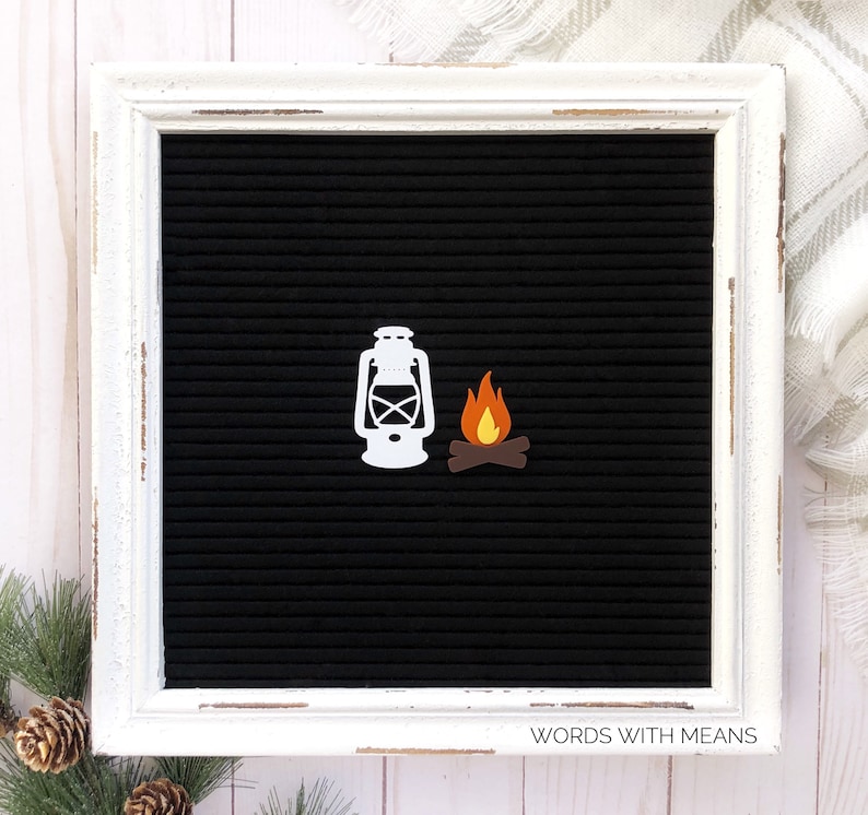 May include: White silhouette of a lantern and a campfire with orange flames on a black letter board with a white frame. The letter board has the text "WORDS WITH MEANS" at the bottom.