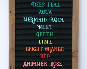 May include: A black letter board with a wooden frame and stand. The board displays the words "Unicorn Purple", "Blue", "Deep Teal", "Aqua", "Mermaid Aqua", "Mint", "Green", "Lime", "Bright Orange", "Red", and "Shimmer Rose".