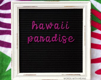 May include: A white framed letter board with a black felt background. The words "hawaii paradise" are spelled out in pink letters.