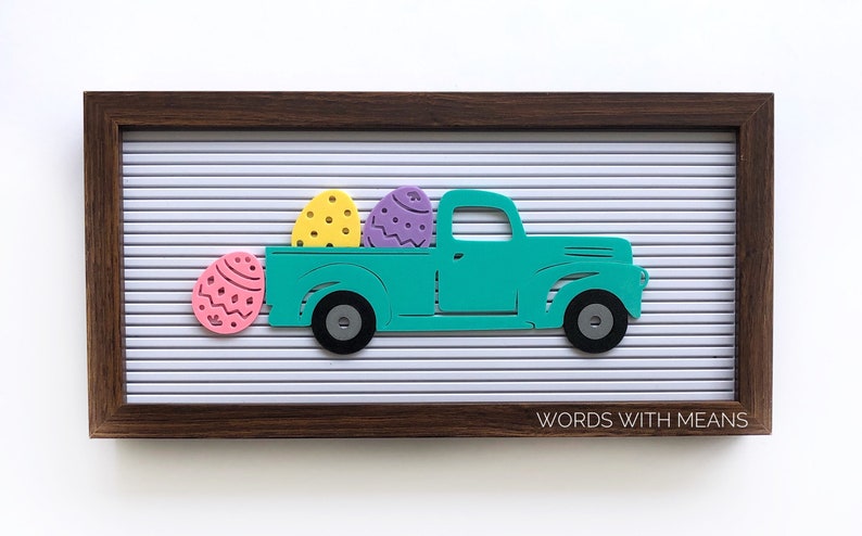 Peut inclure: Un camion de couleur bleu turquoise transportant trois &oelig;ufs de P&acirc;ques jaunes, violets et roses sur un tableau d'affichage blanc avec le texte "WORDS WITH MEANS" dans le coin inf&eacute;rieur droit.