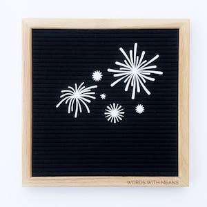 Puede incluir: Un tablero de letras negro con un marco de madera y letras de fieltro blanco que deletrean "WORDS WITH MEANS". El tablero est&aacute; decorado con recortes de papel blanco en forma de fuegos artificiales.