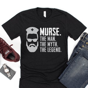 Puede incluir: Camiseta negra con un gr&aacute;fico blanco de un hombre con barba y gafas de sol que lleva un gorro de enfermera. El texto "NURSE. THE MAN. THE MYTH. THE LEGEND." est&aacute; impreso debajo del gr&aacute;fico.
