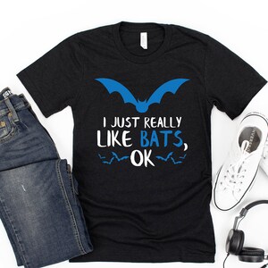 Pu&ograve; includere: Maglietta nera con un'immagine di pipistrello blu e il testo "Mi piacciono davvero i pipistrelli, ok".