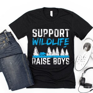May include: Black t-shirt with a white graphic that says "Support Wildlife Raise Boys". The graphic also includes a blue bear and trees.