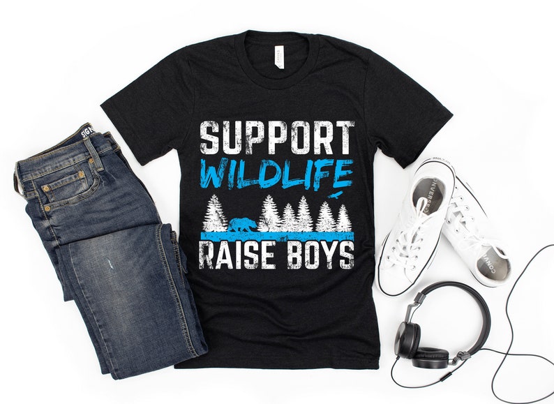May include: Black t-shirt with a white graphic that says "Support Wildlife Raise Boys". The graphic also includes a blue bear and trees.