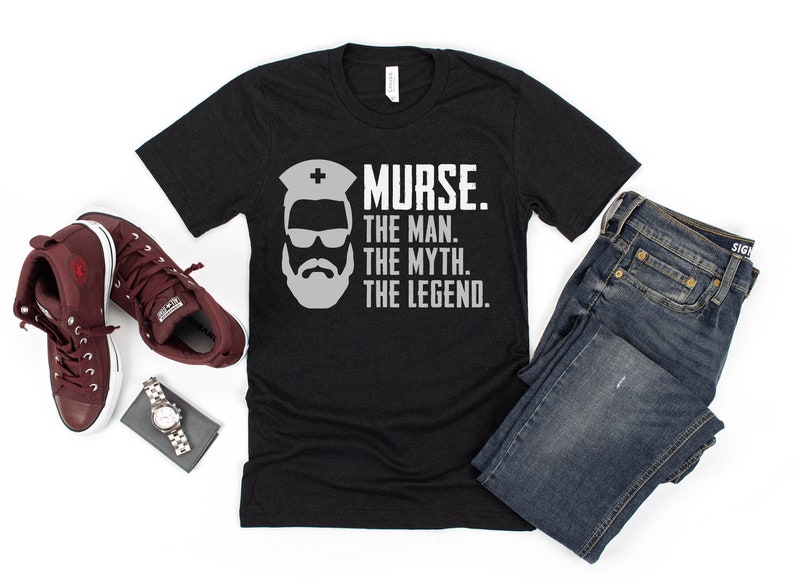 Puede incluir: Camiseta negra con un gr&aacute;fico blanco de un hombre con barba y gafas de sol que lleva un gorro de enfermera. El texto "NURSE. THE MAN. THE MYTH. THE LEGEND." est&aacute; impreso debajo del gr&aacute;fico.