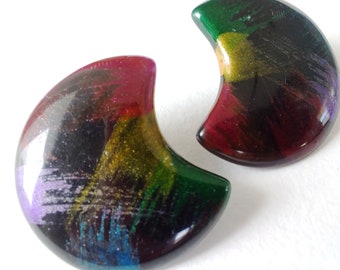 May include: Two crescent-shaped earrings with a glossy finish. The earrings feature a blend of colors, including red, green, purple, and gold, creating a unique, abstract design. The earrings are set against a white background.