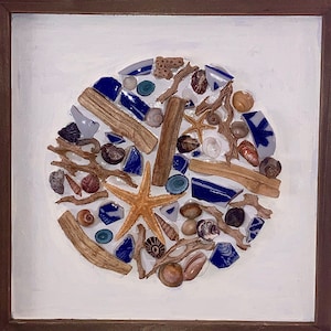 May include: A framed artwork featuring a circular mosaic of seashells, driftwood, and blue and white ceramic tiles. The mosaic is set against a white background and framed in a brown wood frame.