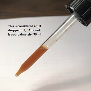 May include: A clear glass dropper with a brown liquid inside. The dropper is full and the text "This is considered a full dropper full. Amount is approximately .75 ml" is visible below the dropper. Photo 3 is also visible in the image.