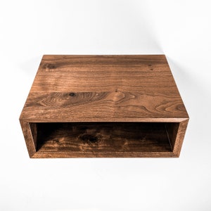 May include: A rectangular, open-front wooden shelf with a rich, dark brown finish. The shelf is mounted on a white wall, showcasing the natural wood grain and the clean lines of the design. The shelf is approximately 24 inches wide.