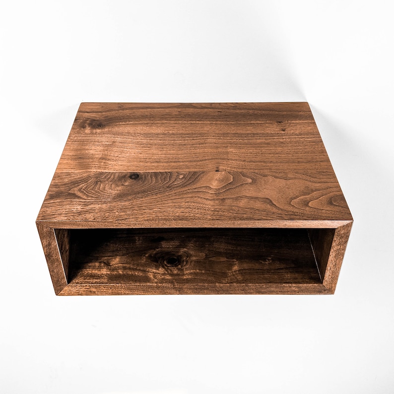 May include: A rectangular, open-front wooden shelf with a rich, dark brown finish. The shelf is mounted on a white wall, showcasing the natural wood grain and the clean lines of the design. The shelf is approximately 24 inches wide.