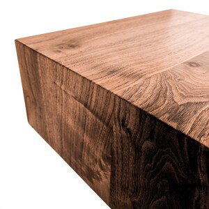 May include: A solid, rectangular wooden block with a rich, dark brown color and visible wood grain. The block's surface is smooth and polished, with a slight sheen. The edges are clean and sharp, suggesting a modern design. This could be a coffee table or a decorative element.