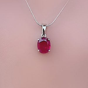 May include: A silver chain necklace with a red oval gemstone pendant.
