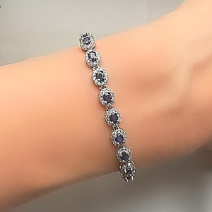 May include: A silver bracelet with a row of oval-shaped blue gemstones surrounded by smaller clear gemstones.