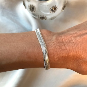 May include: A silver snake chain bracelet on a person's wrist.