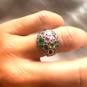May include: A silver ring with a cluster of colorful gemstones set in a marcasite design.