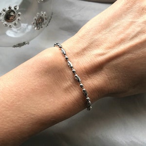 以下が含まれることがあります： 繊細なデザインのシルバーチェーンブレスレット。ブレスレットは、小さな丸いリンクで構成されており、それらが互いに接続されて連続したチェーンを形成しています。