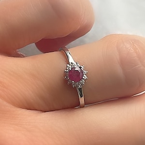Peut inclure: Une bague en argent avec une pierre rouge entourée de petites pierres blanches.
