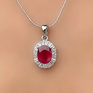 May include: A silver chain necklace with a pendant featuring a large oval-shaped ruby surrounded by a halo of smaller white gemstones.