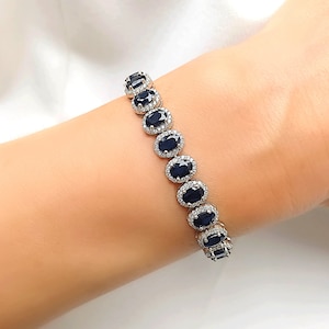 Op de afbeelding: Een zilveren armband met een rij ovale blauwe edelstenen, omringd door kleinere heldere stenen.