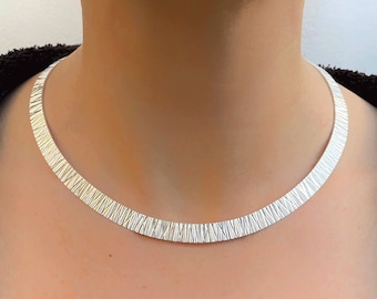 May include: A silver textured choker necklace. The necklace is a simple, minimalist design.