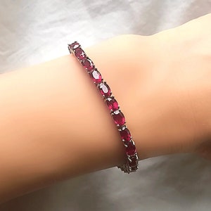 May include: A red gemstone tennis bracelet with oval-shaped stones set in silver.