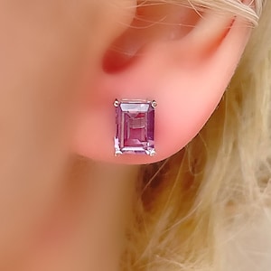 May include: A pair of silver stud earrings with a square, purple gemstone.