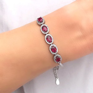 Peut inclure: Un bracelet en argent avec un extenseur de chaîne présente cinq pierres précieuses rouges de forme ovale entourées de pierres précieuses claires plus petites.