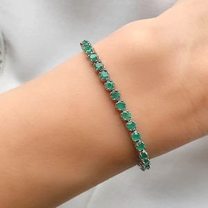 Puede incluir: Un brazalete de tenis de plata con piedras preciosas redondas verdes.