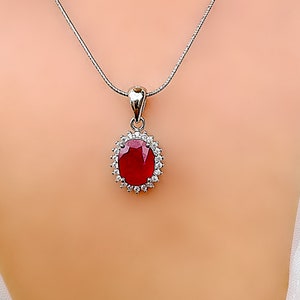 May include: A silver chain necklace with a pendant featuring a large oval-shaped ruby surrounded by smaller white diamonds.
