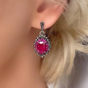 Puede incluir: Pendientes de plata con un gran gemas rosa rodeado de piedras más pequeñas brillantes.