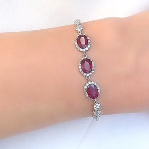 May include: A silver bracelet with three oval-shaped red gemstones surrounded by smaller white gemstones.