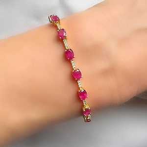 May include: A gold bracelet featuring a line of oval red gemstones and small clear stones.