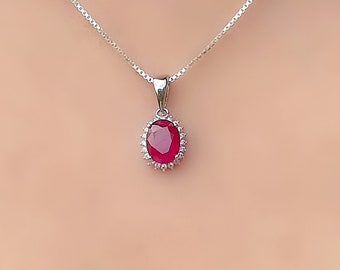 May include: A silver chain necklace with a red oval gemstone pendant surrounded by smaller clear gemstones.