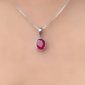 May include: A silver chain necklace with a red oval gemstone pendant surrounded by smaller clear gemstones.