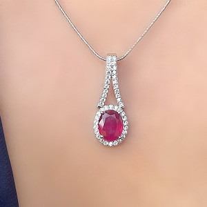 May include: A silver necklace with a pendant featuring a large oval ruby surrounded by smaller diamonds.