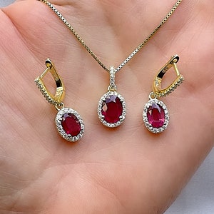 May include: A gold necklace and earrings set featuring a red oval gemstone surrounded by smaller clear gemstones.