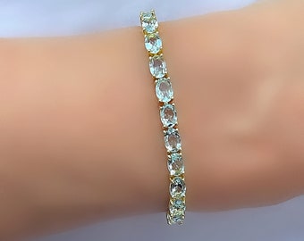 May include: A gold tennis bracelet with oval-shaped aquamarine gemstones.