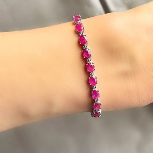 May include: A silver bracelet with a row of oval-shaped pink gemstones.