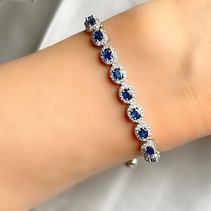 May include: A silver bracelet featuring oval-shaped, deep blue gemstones surrounded by smaller, clear stones. The bracelet is displayed on a person's wrist, showcasing its design and sparkle. The bracelet is a piece of jewelry.